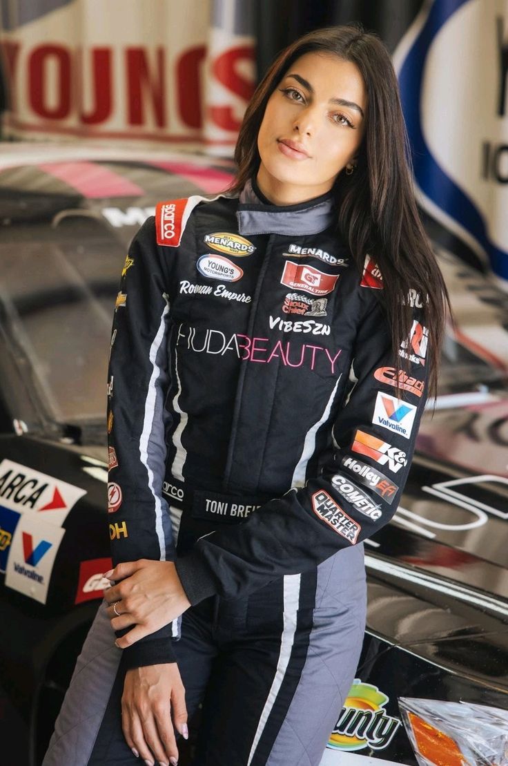 a beautiful young woman standing next to a racing car