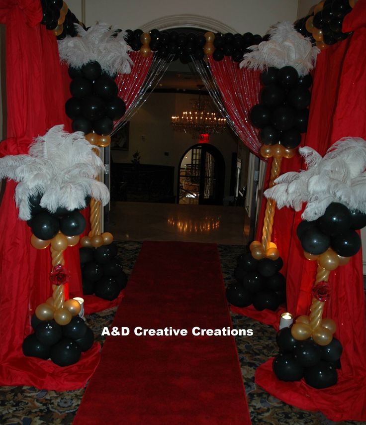 a red carpeted hallway decorated with black and gold balloons, white feather boa