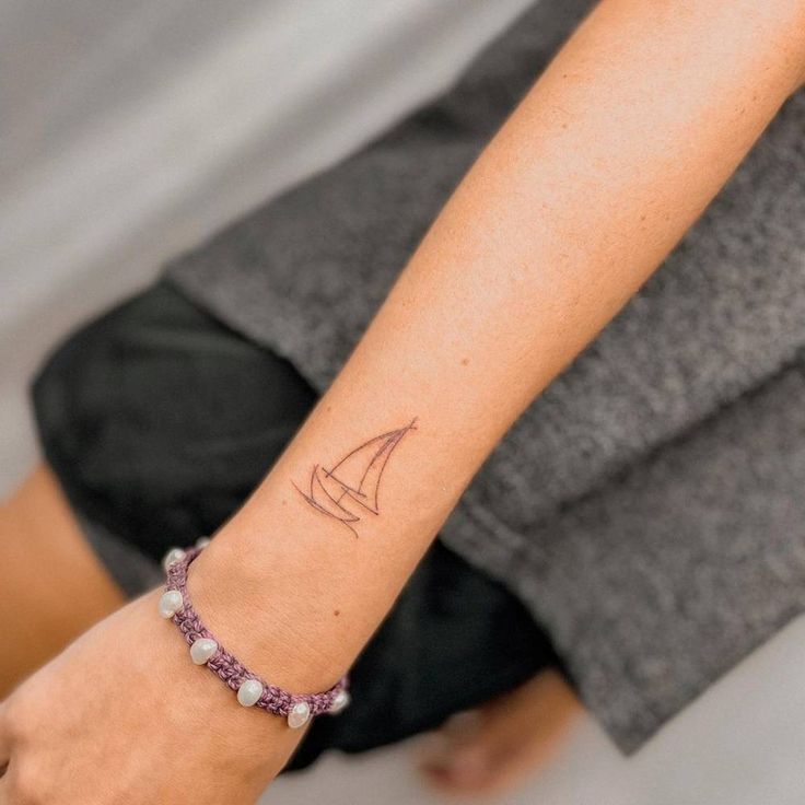 a woman's arm with a small sailboat tattoo on her left wrist and a pink beaded bracelet