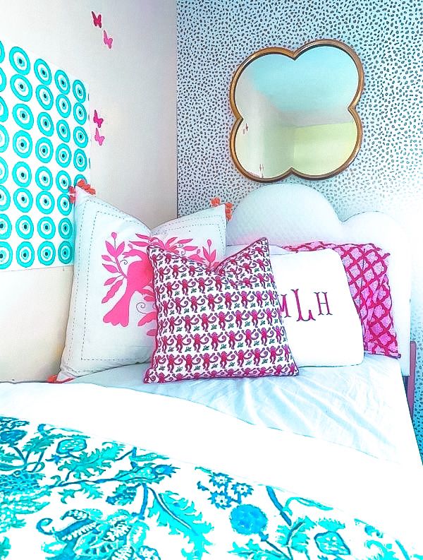 a bed with blue and pink pillows on top of it next to a white wall