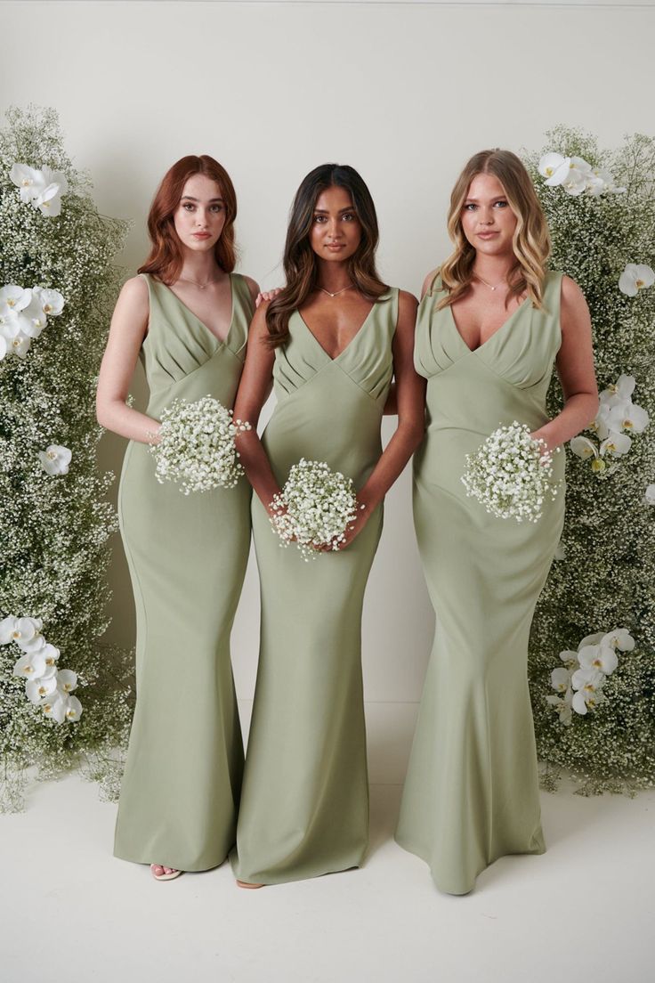 three women in long dresses standing next to each other with flowers on their backs and one woman holding a bouquet