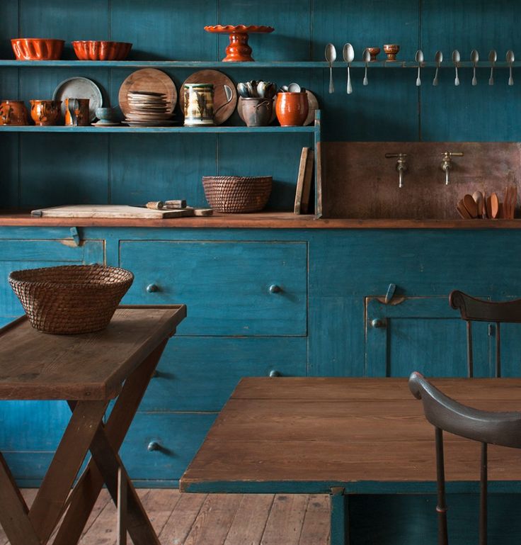 a kitchen with teal cabinets and wooden tables in front of the counter top is filled with bowls, plates and utensils