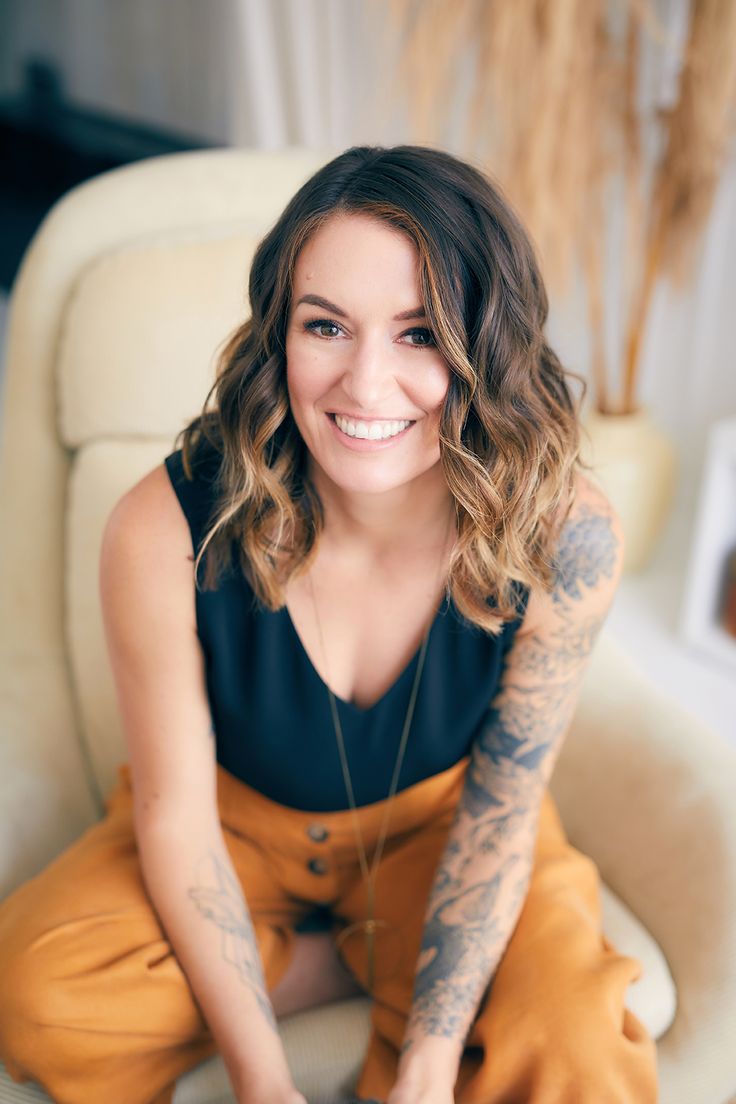 a woman sitting in a chair with her legs crossed and tattoos on her arm, smiling at the camera