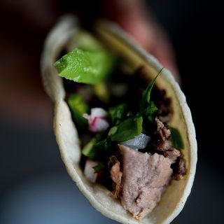 a hand holding a taco filled with meat and veggies