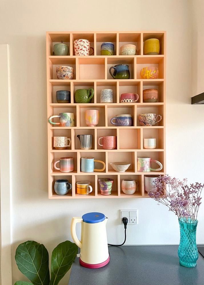 a wooden shelf filled with cups and vases on top of a counter next to a wall mounted potted plant