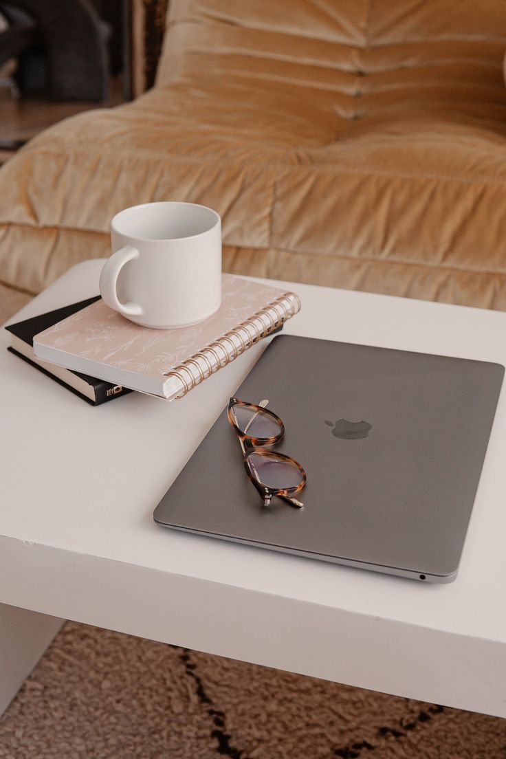 an apple laptop computer sitting on top of a white table next to a coffee cup