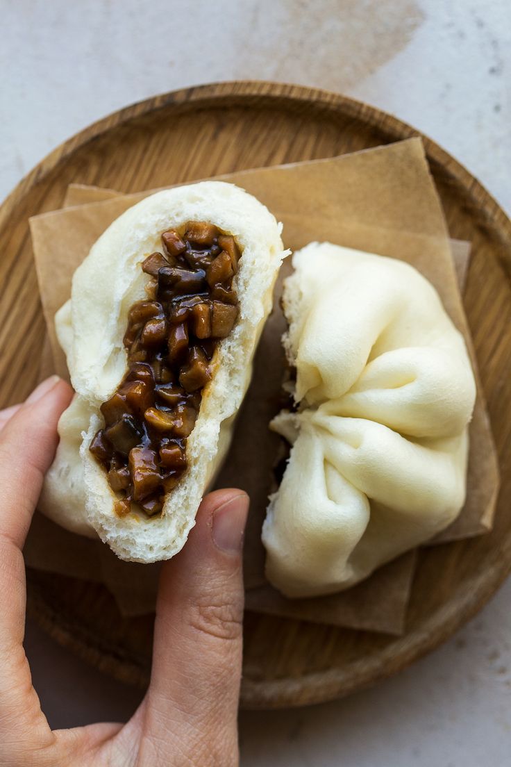 a person holding a bun with some food on it