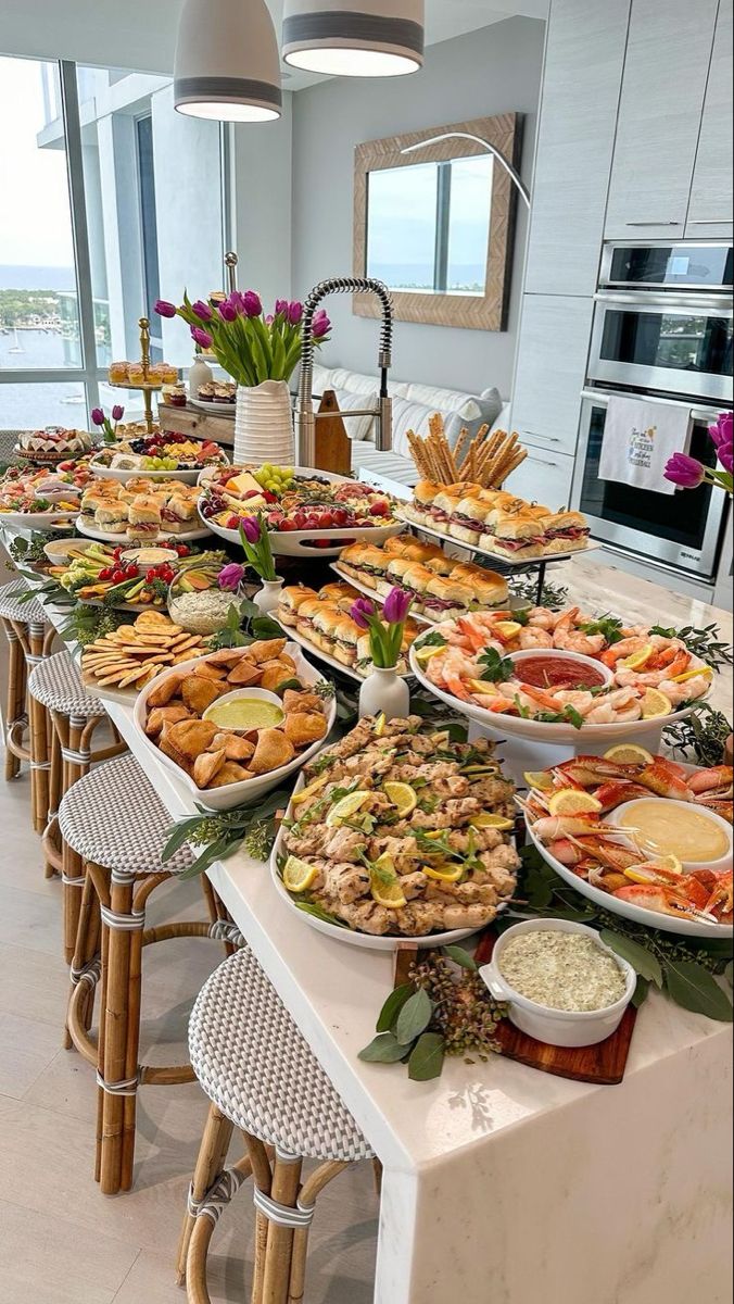 a long table filled with lots of food on top of a white counter next to a window