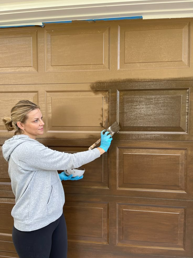 a woman is painting the side of a garage door with blue gloves on her hands