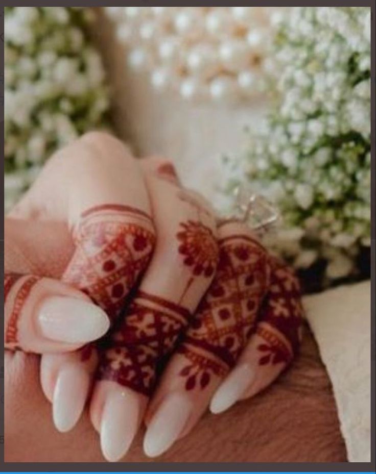 two hands holding each other with henna tattoos on their fingers and arms, both decorated with flowers