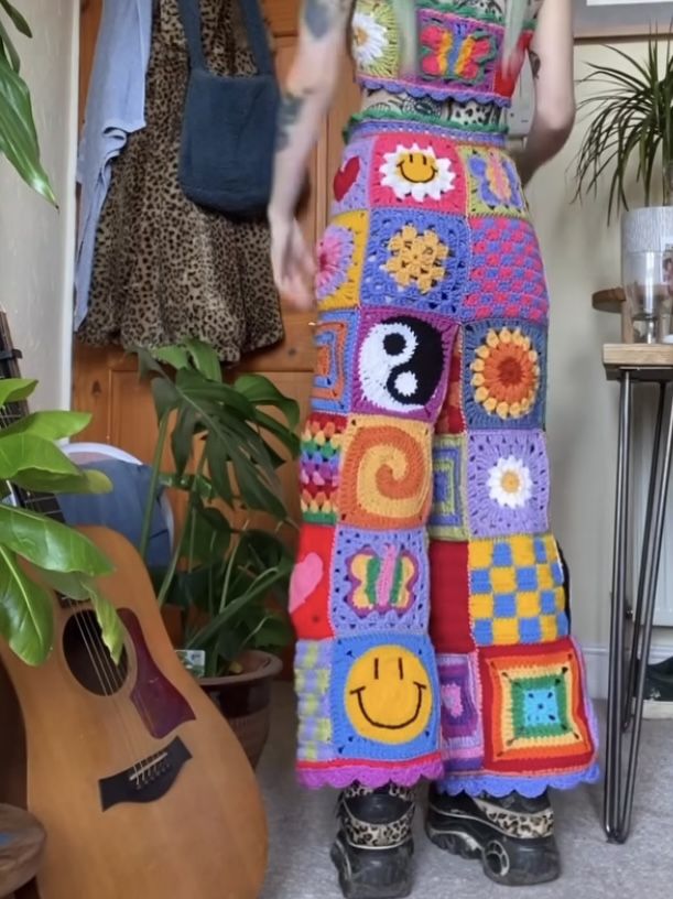 a woman standing in front of a guitar wearing a multicolored crocheted skirt