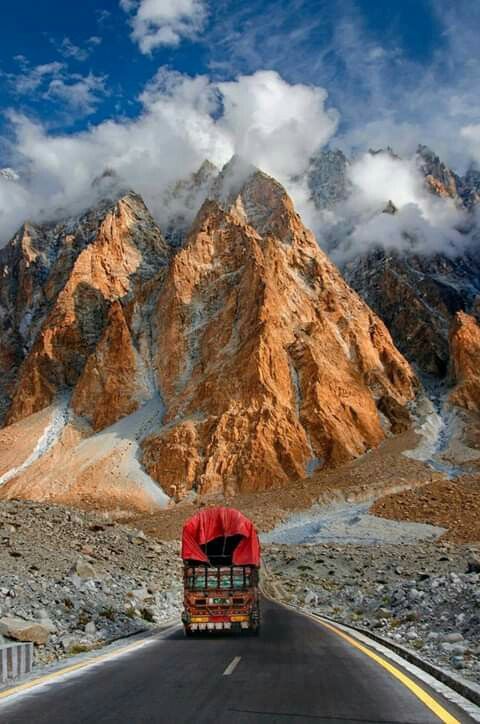 a truck is driving down the road in front of some snow covered mountains and clouds