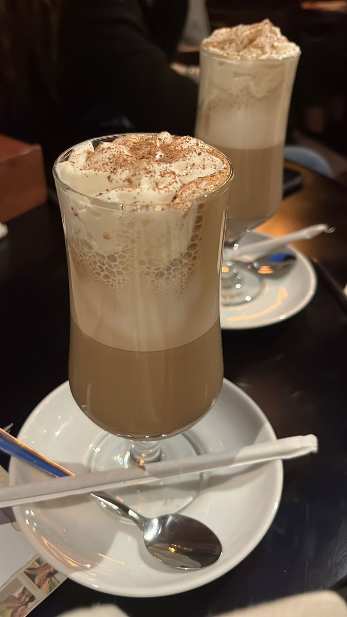 two glasses filled with ice cream sitting on top of a table next to silverware