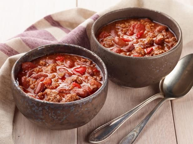 two bowls filled with chili and meat on top of a wooden table next to spoons