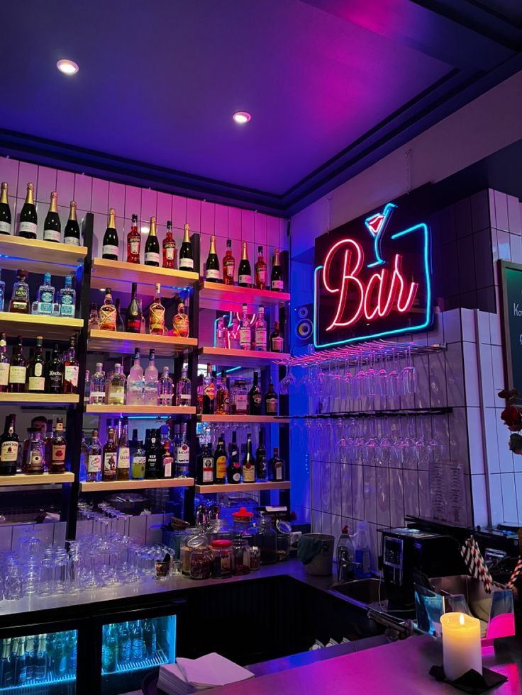 the bar is filled with many different types of liquors and drinks on shelves, along with neon lights