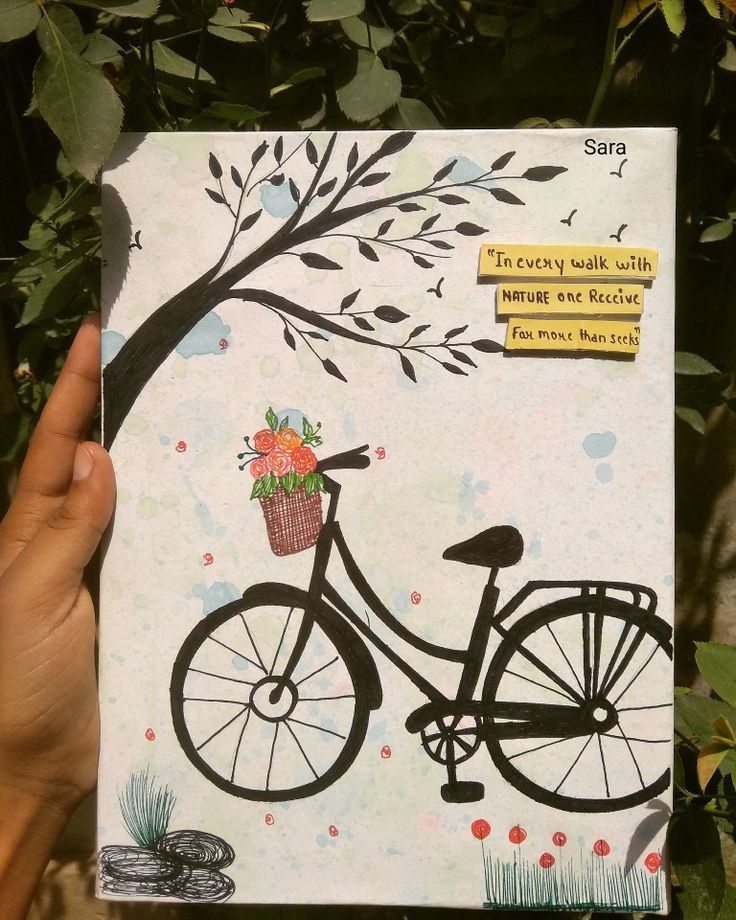 a hand holding up a card with a bicycle and flowers on it, in front of some trees