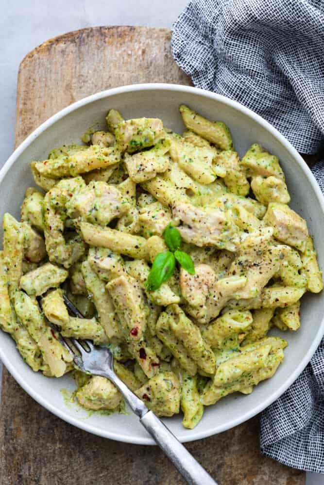 a white bowl filled with pasta and pesto on top of a wooden cutting board