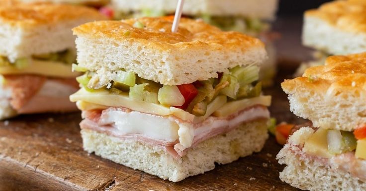 sandwiches with meat, cheese and vegetables are on a cutting board next to toothpicks