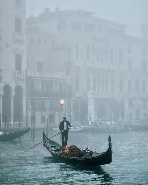 a man in a gondola on a foggy canal with buildings behind him