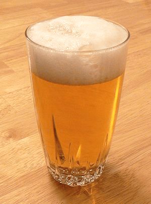 a glass filled with beer sitting on top of a wooden table