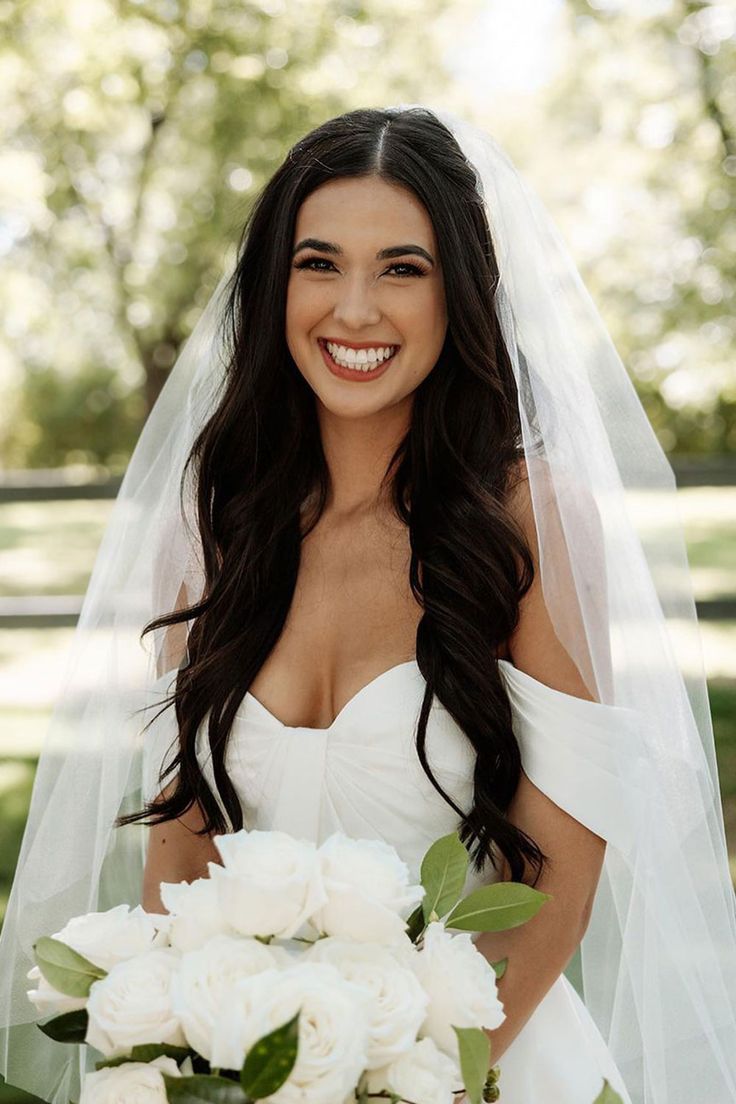 a woman in a white wedding dress holding a bouquet of flowers and smiling at the camera