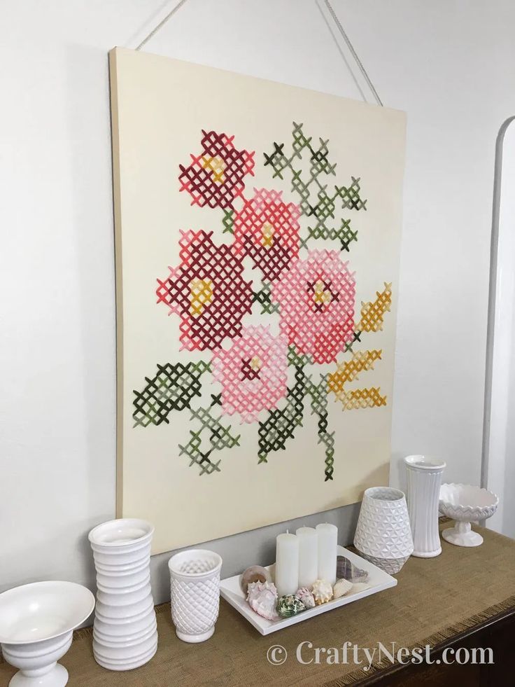 a cross - stitch floral arrangement is displayed on the wall next to plates and cups