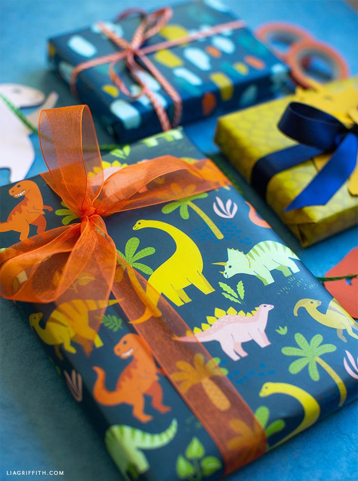 three wrapped presents with colorful wrapping paper and orange ribbon on blue table cloth, decorated with dinosaurs