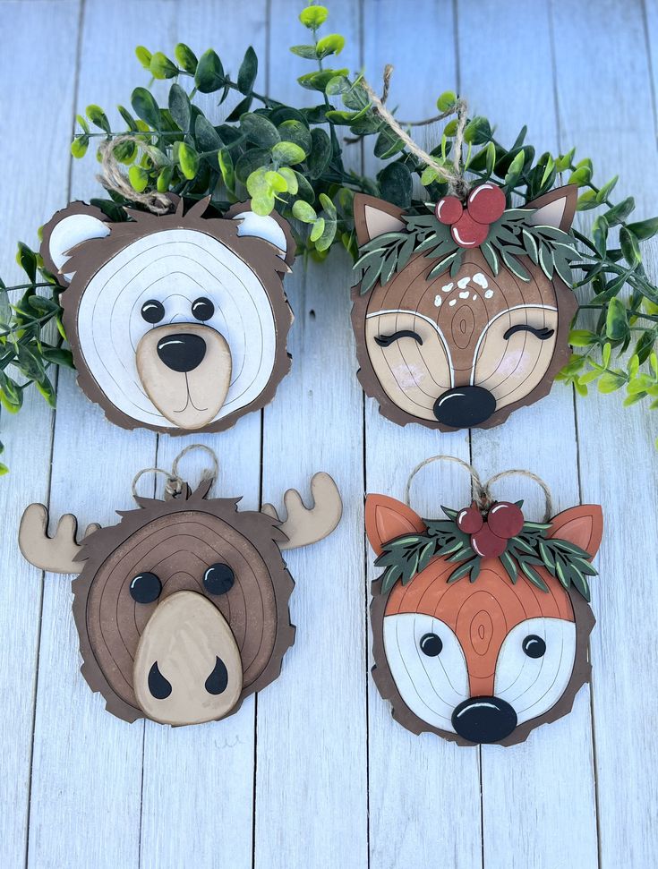 four wooden animal ornaments are hanging on a white wood background with green leaves and branches