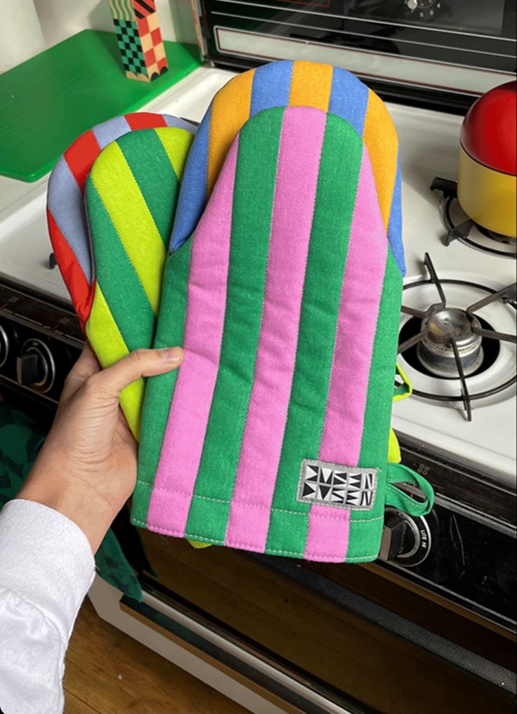 the oven mitt is colorfully striped and has a hand holding it