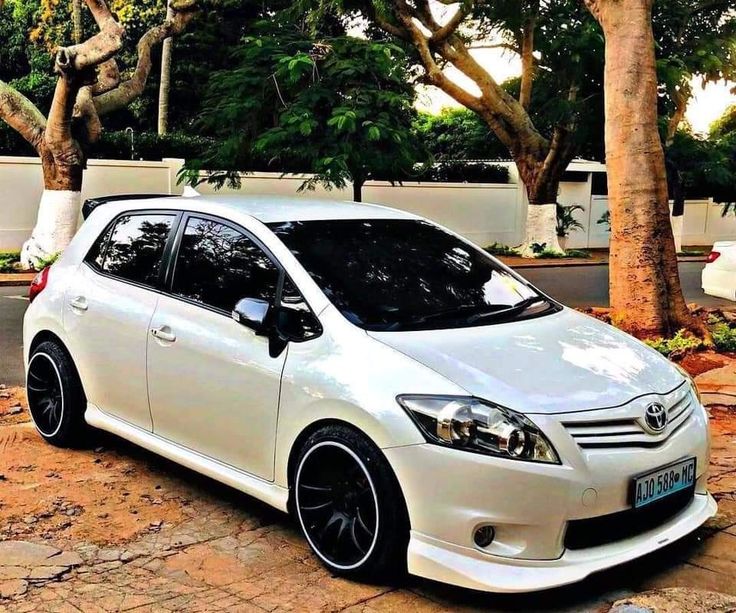 a white toyota car parked in front of some trees and bushes on the side of the road