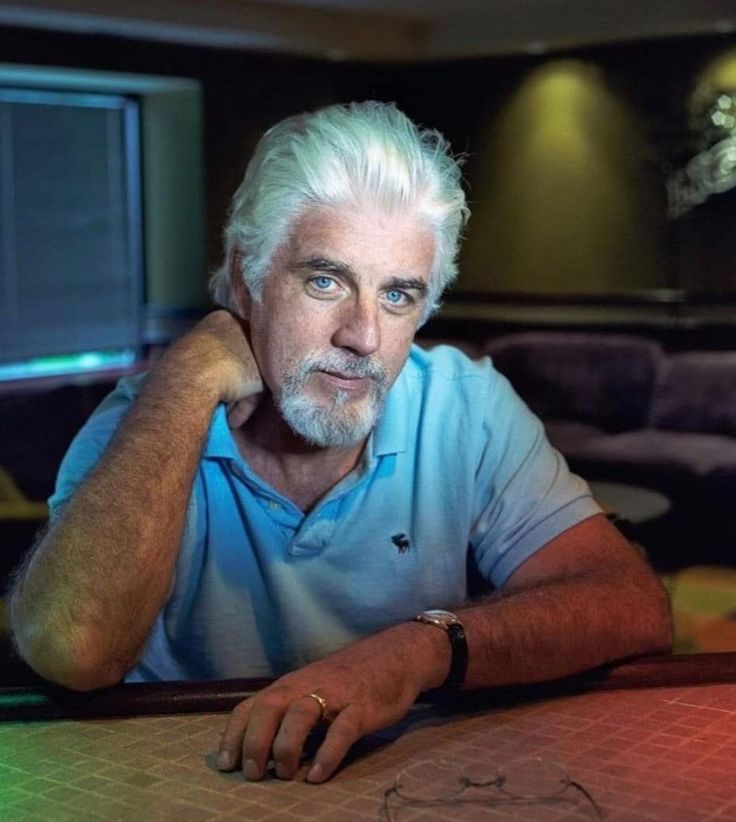 an older man sitting at a table with his hand on his chin and looking off to the side