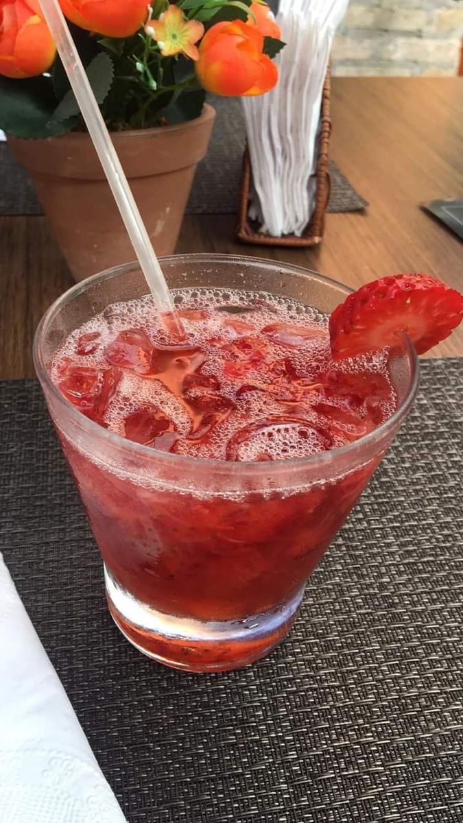 a glass filled with ice and strawberries on top of a table next to a potted plant