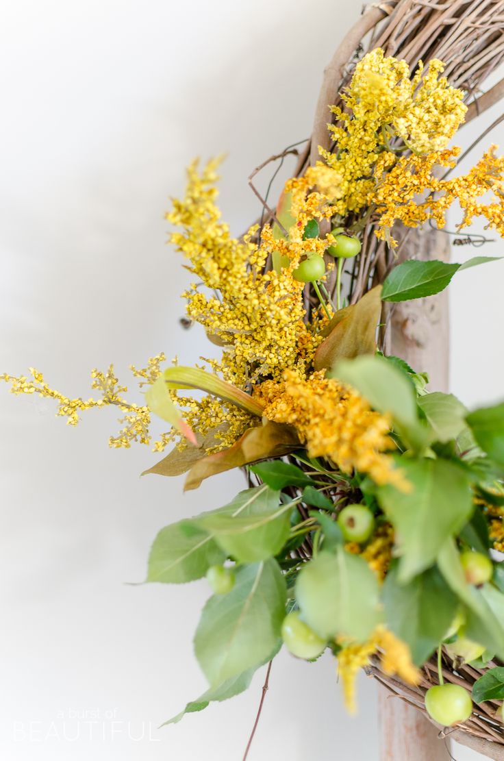 a wreath with yellow flowers and greenery hanging from the front of a wooden door