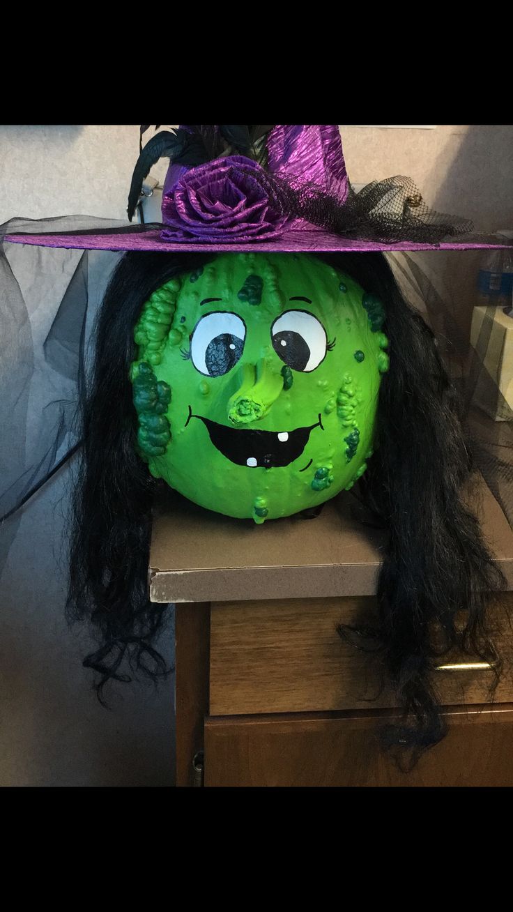 a green pumpkin with black hair wearing a purple hat on top of it's head