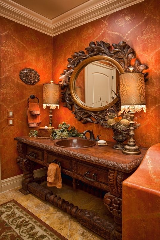 a fancy bathroom with orange walls and marble counter tops, an ornate mirror above the sink