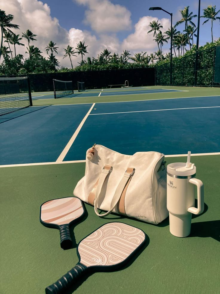 a tennis court with a bag, racquet and two cups on the ground