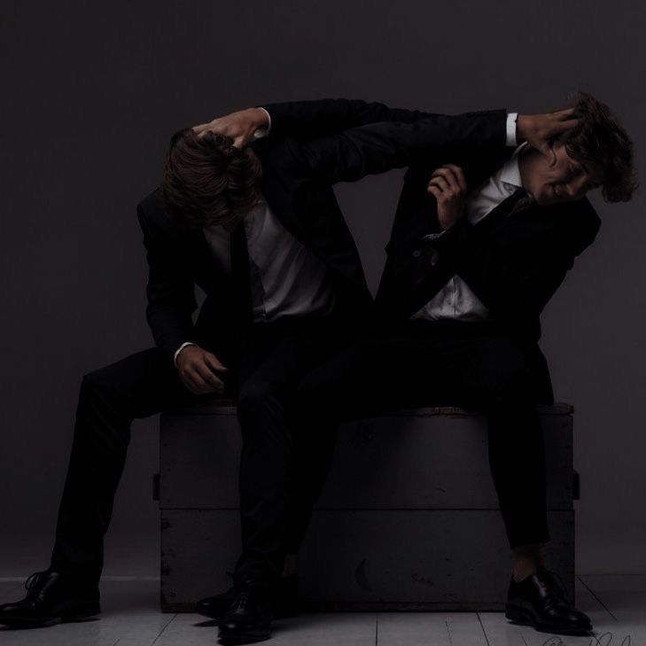 two men in suits sitting on top of a box with their arms around each other