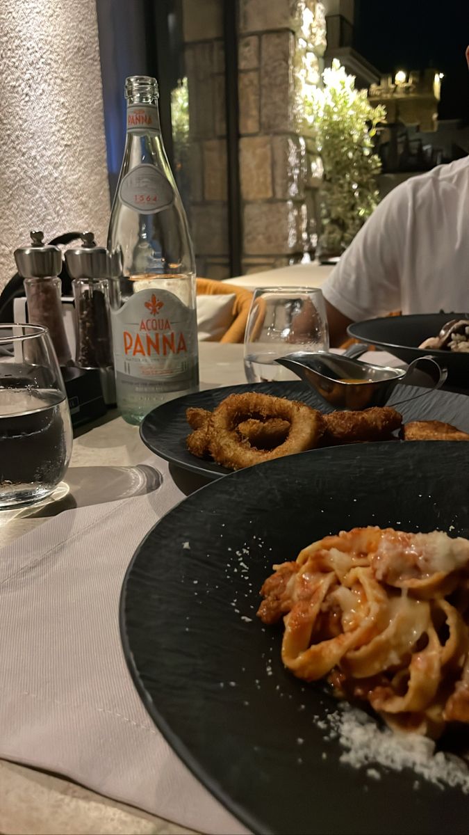 two plates with food on them sitting on a table next to a bottle of wine