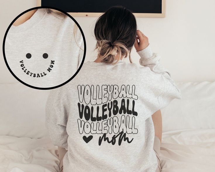 a woman sitting on top of a bed wearing a white shirt with the words volleyball written across it