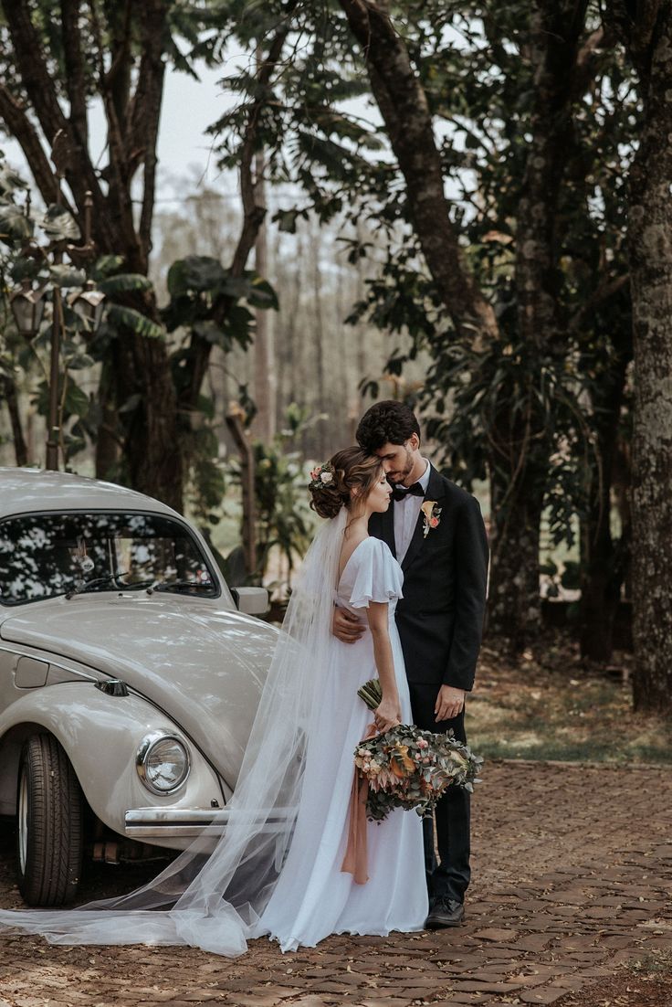 a bride and groom standing next to an old car