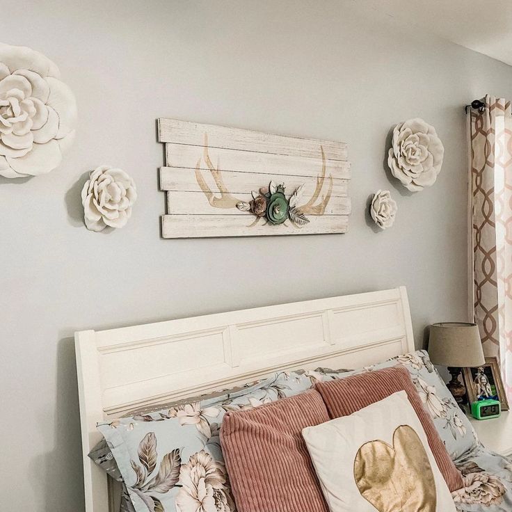 a white bed topped with lots of pillows next to a wall covered in pictures and flowers