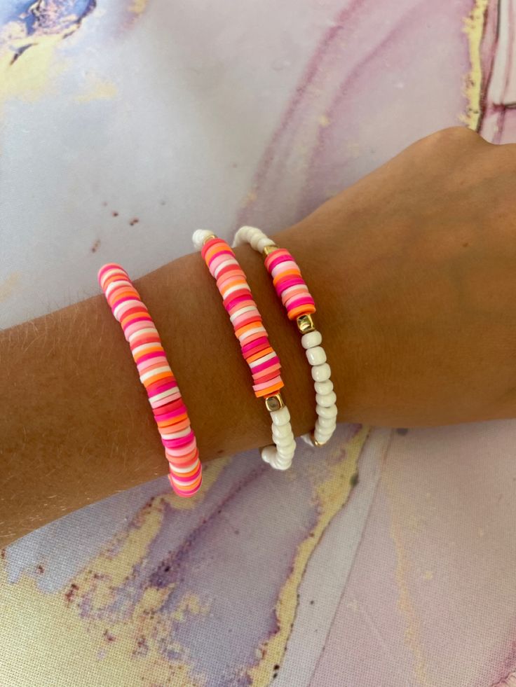 three bracelets on the arm of a person wearing a pink and white striped shirt