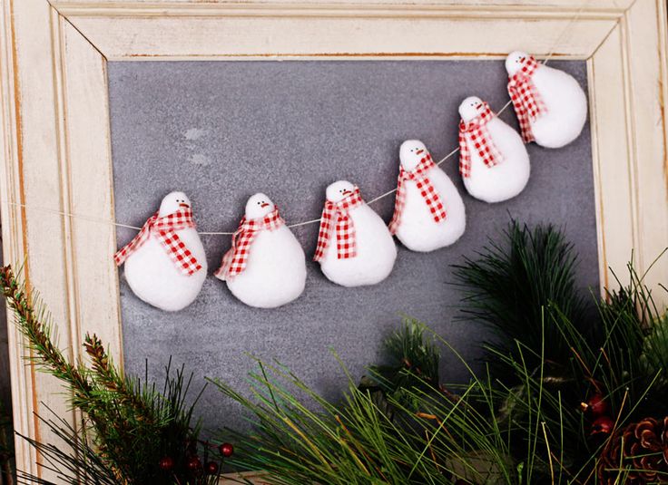 snowmen are hanging on a string in front of a chalkboard with pine branches