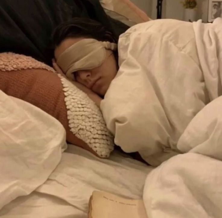 a woman sleeping in bed with blindfolds on her head and an open book