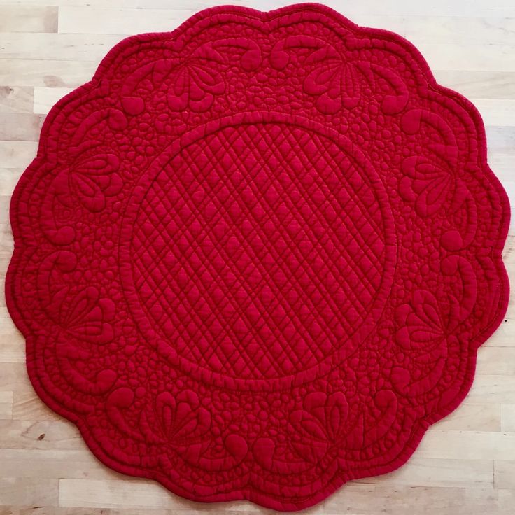 a red placemat with an intricate design on the center and sides, sitting on a wood floor