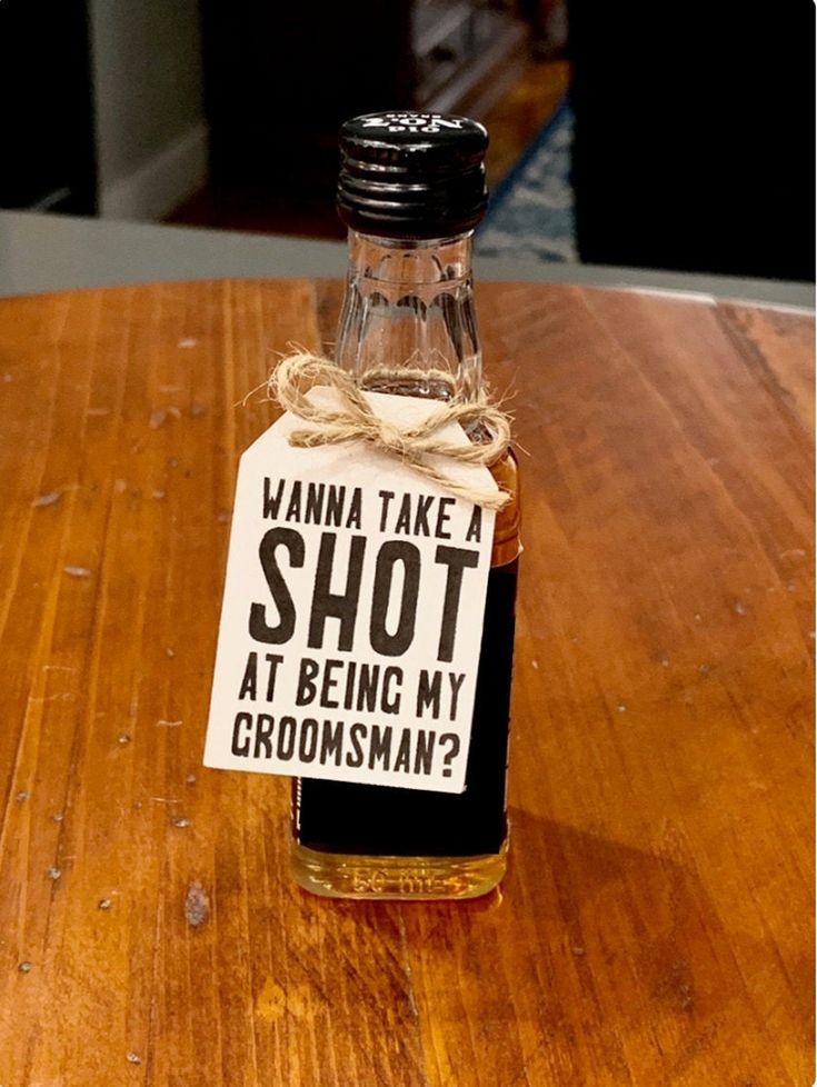 a bottle of whiskey sitting on top of a wooden table next to a sign that says, wanna take shot at being my groomsman?