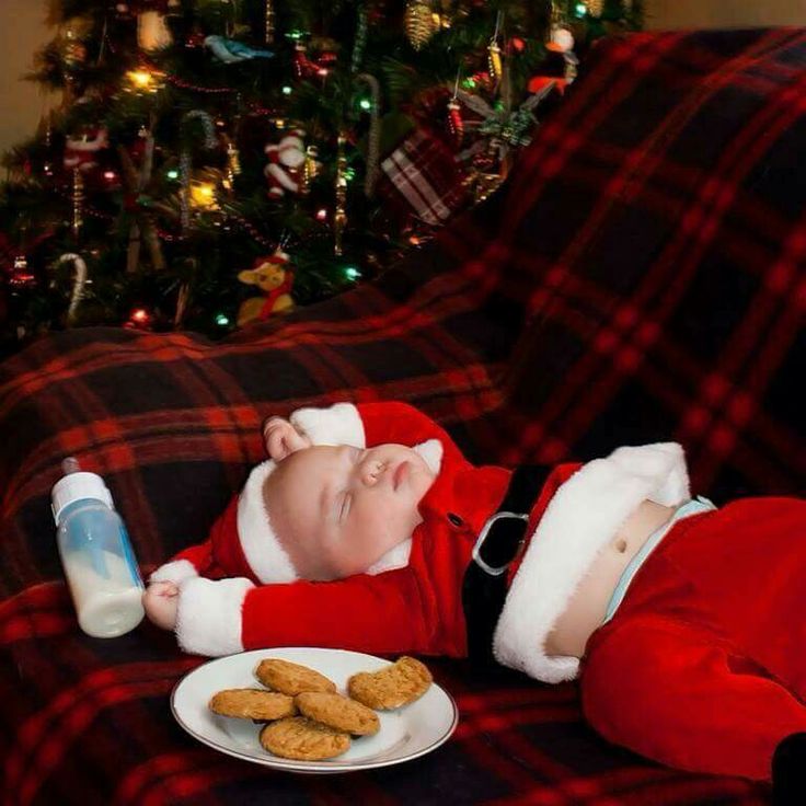 a baby dressed as santa claus laying on a couch next to cookies