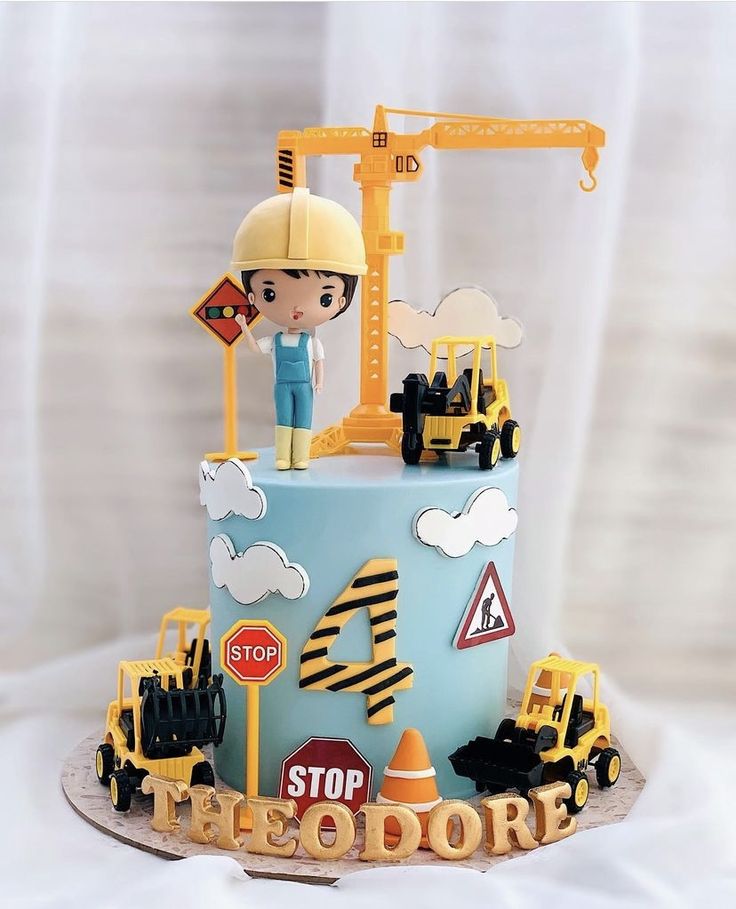 a blue cake with construction themed decorations on it's sides and a boy in a hard hat standing at the top