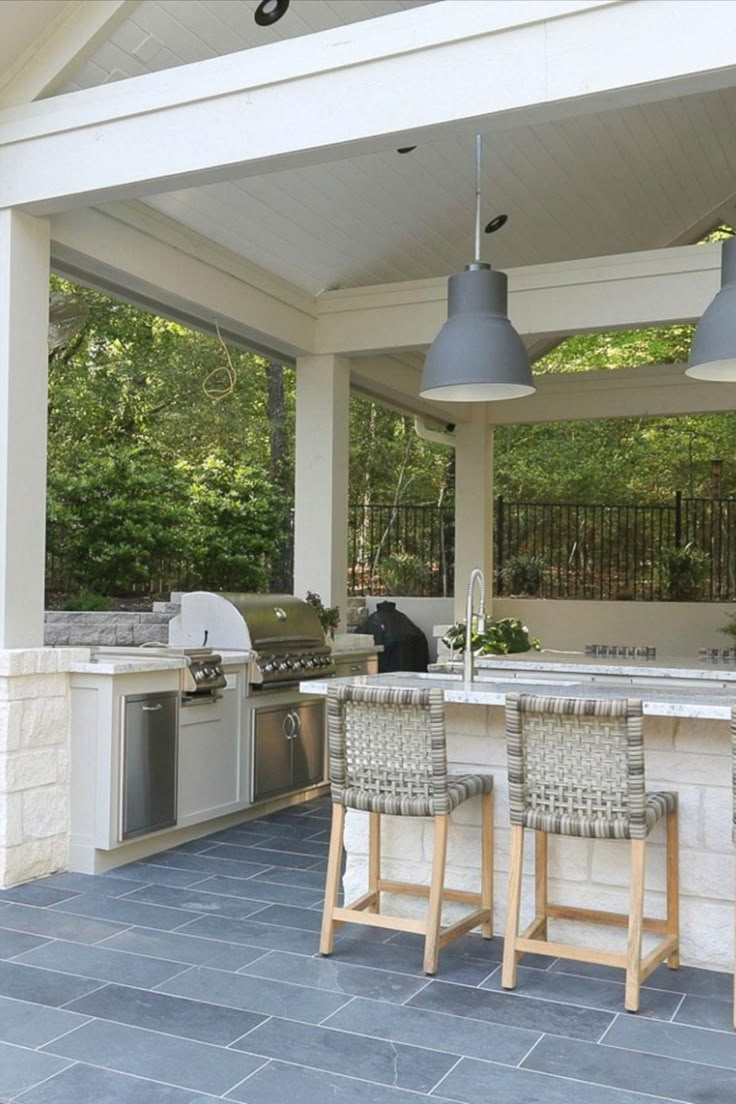 an outdoor kitchen with two bar stools on the counter and three lights hanging from the ceiling