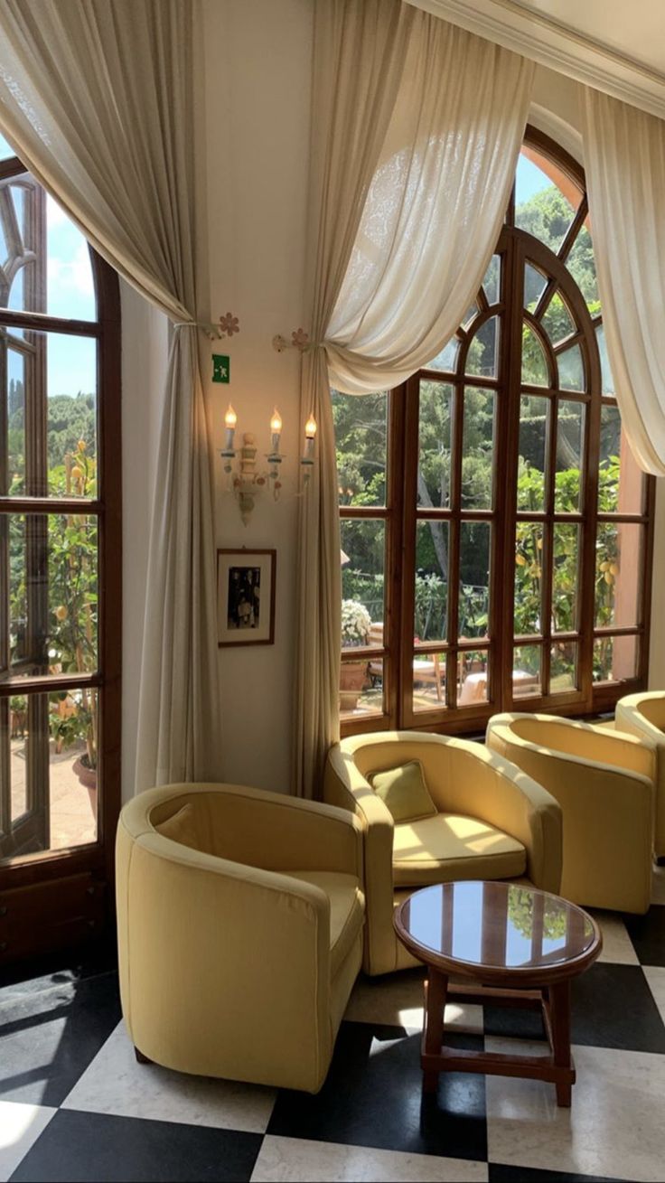 a living room filled with lots of furniture and large windows covered in white drapes